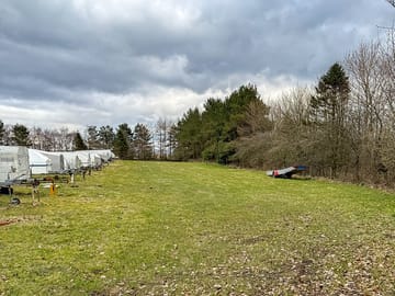 Looking down the motorhome pitches, between the trailers and the road behind the trees