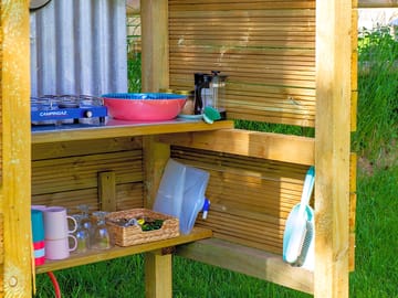 Outdoor under cover kitchen equipped with crockery, cutlery, glasses, frying pan, saucepan