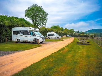 Photo of the site, the pitching areas, the outdoor dining benches and the surrounding hills