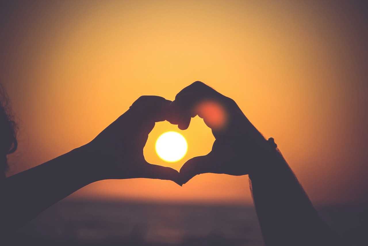 Silhouette of two hands forming a heart around a sunset